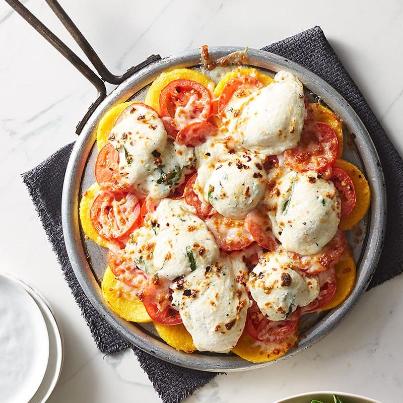 a 10-inch round pizza pan filled with polenta slices that have been topped with a 3-cheese mixture and tomato slices