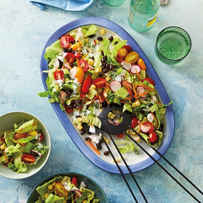Large rectangular serving dish filled with a chopped salad of lettuce, tomatoes, black beans, corn, radishes, and scallions tossed with a creamy dressing
