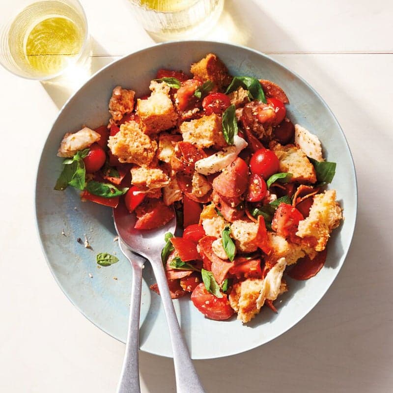 Large gray serving bowl filled with chopped tomatoes, toasted bread, turkey pepperoni, fresh mozzarella, and basil, tossed with a vinaigrette